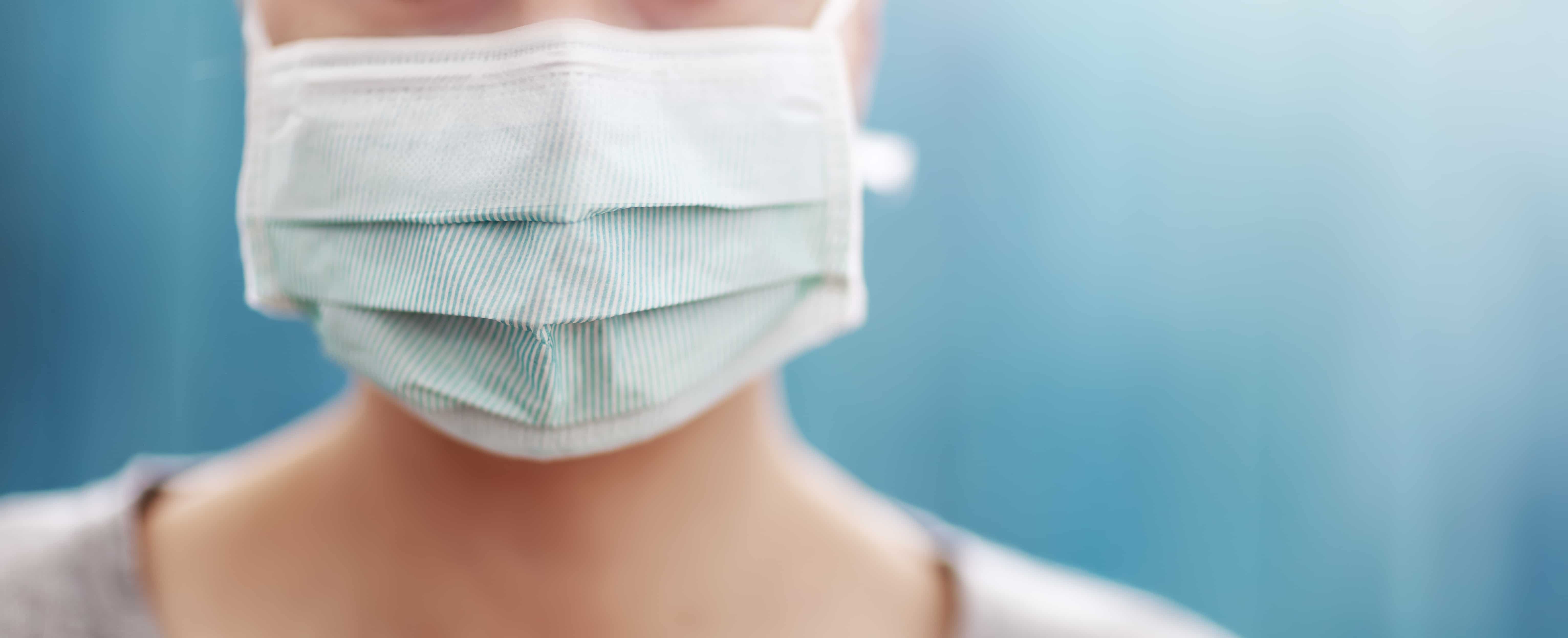 young woman in medical face protection mask indoors on blue background